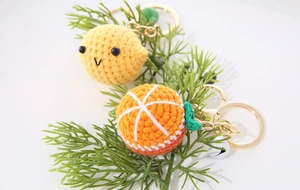 Macro shot of handmade crochet citrus fruit keychains with leaf detail and gold chain