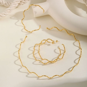 Detailed close-up of golden wavy stainless steel jewelry set including necklace and bracelet
