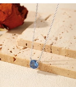 Macro shot of silver necklace with round sapphire blue pendant on textured stone
