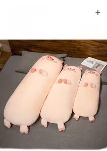 Detailed view of three sizes of soft pink plush pig bolsters on a cozy grey bed