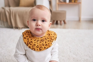 Close-up of a baby wearing a yellow leopard print cotton bib in a cozy home setting