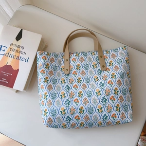 Détails d'un sac cabas en coton fleuri avec poignées en cuir kaki et rivets renforcés