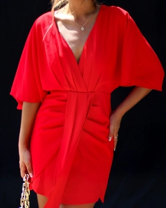 Détail d'une robe rouge à col en V profond avec plis à la taille et manches chauve-souris