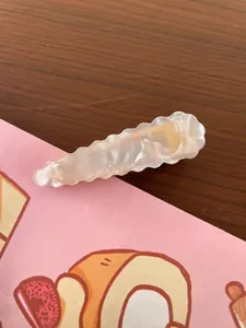 Detail showing wavy cream hair clip with pearlescent finish on decorative background