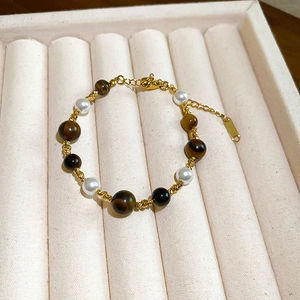 Detailed shot of tiger eye beads and pearls bracelet with gold plated accents on beige velvet