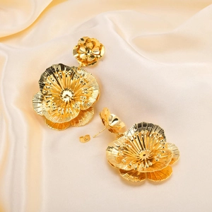Detailed view of oversized golden flower earrings on premium silk fabric background