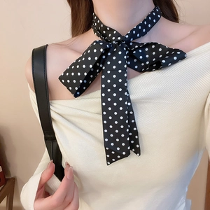 Dettaglio ravvicinato di un foulard in seta a pois neri e bianchi annodato come cravatta chic