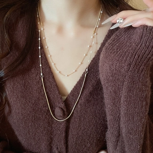 Detail of layered gold snake chain necklace with small white pearls on a model