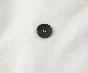 Close-up of a classic black resin button on soft light beige wool fabric texture
