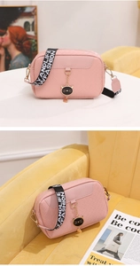 Pink woven camera bag detail with cat charm and stylish wide crossbody strap