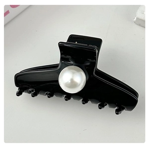 Detail shot of a black glossy hair claw clip featuring a large elegant pearl ornament