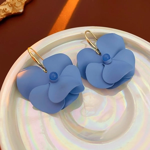 Detailed view of light blue multi-layered petal flower earrings on a white pearl dish