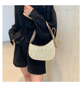Detail of woven beige bag with floral embroidery and bow accent shown on shoulder