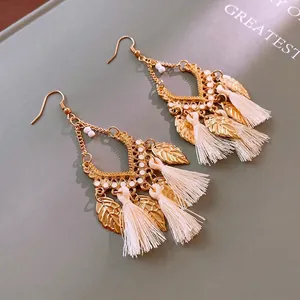 Bohemian gold leaf tassel drop earrings with white beads and hooks on a soft green background
