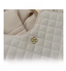 Détail du sac cabas matelassé blanc cassé avec logo floral doré et texture en losanges