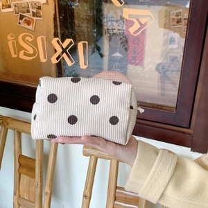 Detail of cream corduroy cosmetic bag with brown polka dots held by hand outdoors