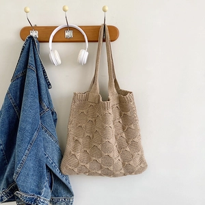 Close-up of beige knitted shoulder bag with hollow butterfly pattern on a wall hook