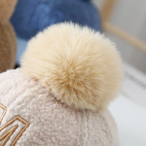 Detailed close-up of soft beige teddy velvet texture and fluffy faux fur pom-pom on top