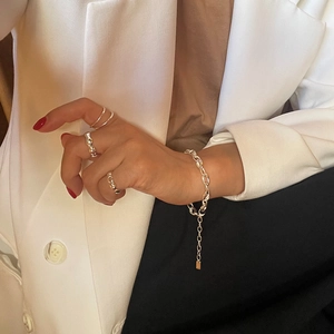 Detail of minimalist silver ring and oval link bracelet worn over a brown shirt