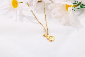 Détail d'un pendentif guitare doré sur chaîne en O, tissu blanc et décor de marguerite