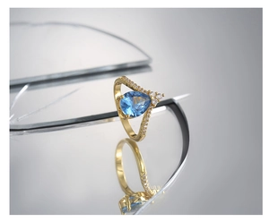 Macro shot of gold V-shaped ring with pear-cut blue zircon and diamond pavé accents
