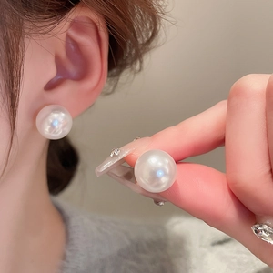 Close-up of a white round pearl stud earring worn on ear, showing glossy finish