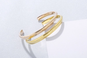 Close-up of gold and rose gold C-shaped bracelets with ONE LIFE ONE LOVE engraving