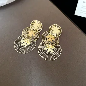Détail macro de boucles d'oreilles dorées à trois niveaux avec motifs franges radiaux