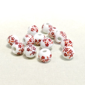 Close-up of 10mm ceramic beads with red floral patterns on white porcelain surface