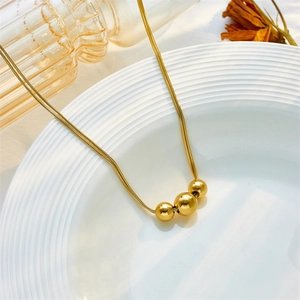 Collana minimalista a catena snake dorata con tre sfere lucide su vassoio in ceramica bianca