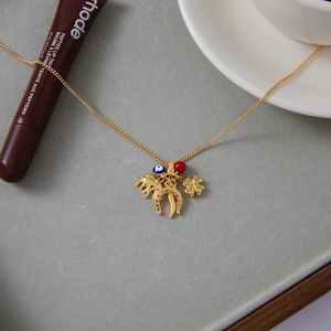 Detail of gold evil eye necklace with elephant, horseshoe, and clover charms on stone tray