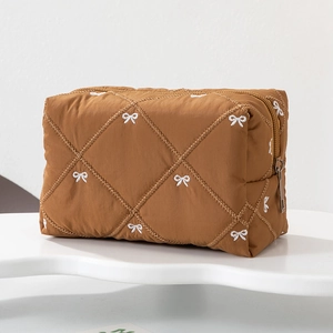 Detail showing brown quilted makeup bag with white bow embroidery and metallic zipper