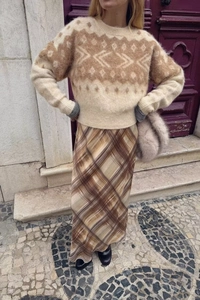 Street style shot of a woman in a beige geometric knit sweater and a plaid midi skirt