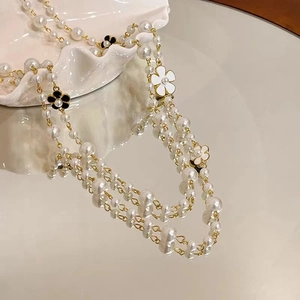 Detail of layered pearl necklace with black and white floral enamel charms on gold chain