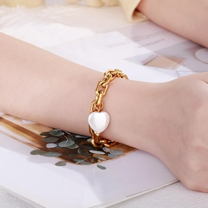 Nahaufnahme eines goldenen Gliederkettenarmbands mit weißem Herzanhänger am Handgelenk