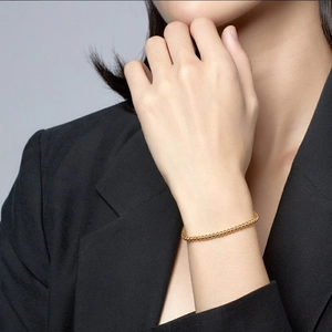 Detail of elegant gold beaded bracelet on model wrist wearing a black blazer jacket