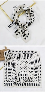 Detail of a cream square silk scarf with black geometric patterns and satin texture