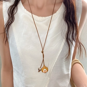 Dettaglio della collana in corda intrecciata con ciondolo a forma di bambina e perline