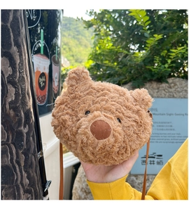 Hand holding a cute brown plush teddy bear head crossbody bag in an outdoor setting
