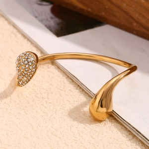 Detail of 18K gold teardrop bangle featuring white rhinestones and polished finish