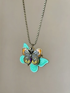 Detail of vintage bronze butterfly pendant with green enamel wings and purple crystals