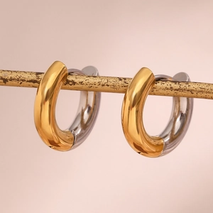 Macro detail of two-tone gold and silver C-shaped stainless steel earrings on a gold rod