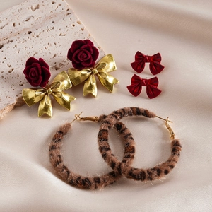 Dettaglio di orecchini a fiocco floreale rosso e cerchi leopardati su seta beige