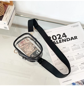 Transparent PVC crossbody bag with black adjustable strap and gold hardware on glass desk