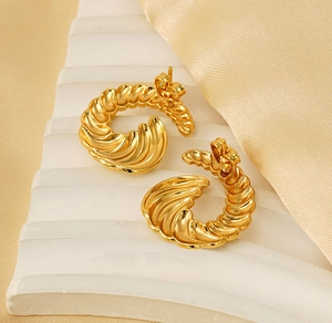Macro view of gold-plated spiral horn textured hoop earrings on premium silk fabric