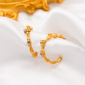 Macro shot of 18k gold plated C-shape earrings with zircon inlay on silk background