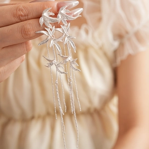 Detail of silver bamboo leaf earrings featuring long tassels and unique metallic finish