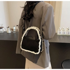 Close-up of black suede shoulder bag with white fleece trim worn in a cafe setting