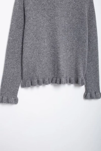 Detail of grey knitted sweater showing soft wool texture and ruffle trim on hem and cuffs