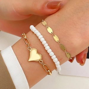Close-up of a three-piece gold heart charm bracelet set with white beads on a woman's wrist